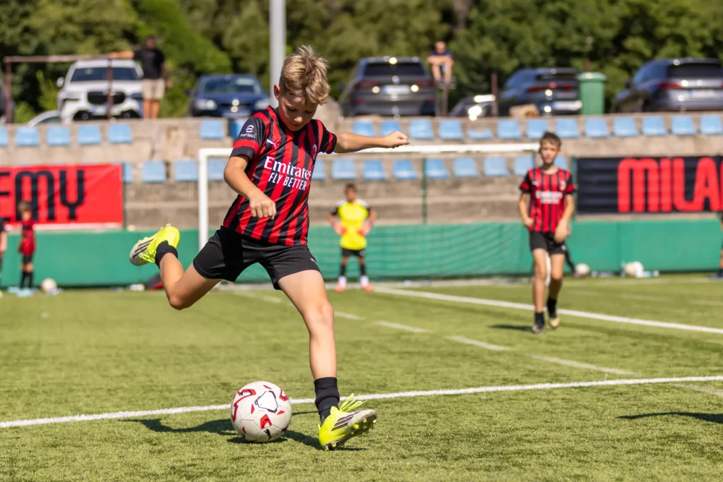 Boy in an AC Milan Academy kit swinging his leg to kick the ball