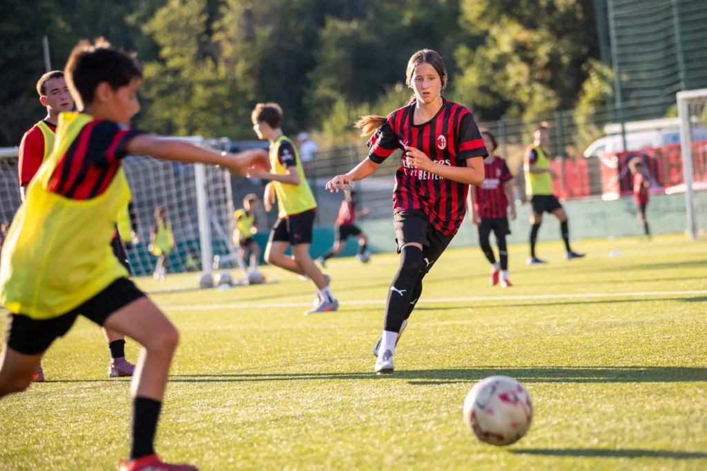 Girl in a red and black AC Milan kit running towards the ball during a training game