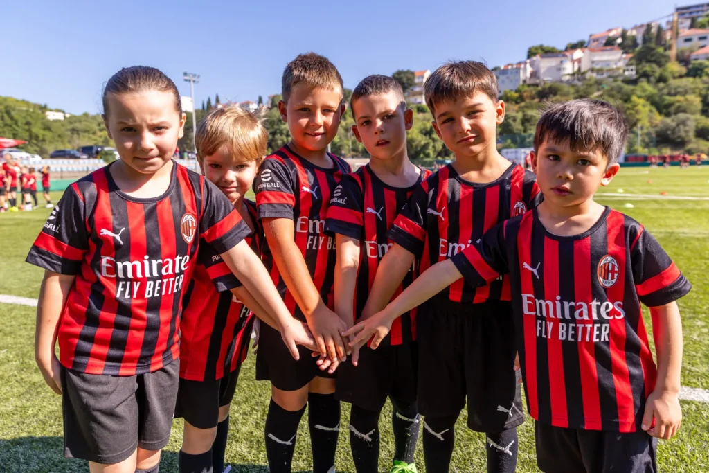 Six young players in AC Milan kits smiling at the camera with their hands stacked together