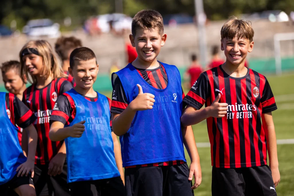 Smiling boys giving a thumbs up, one in a blue training bib and one in an AC Milan kit