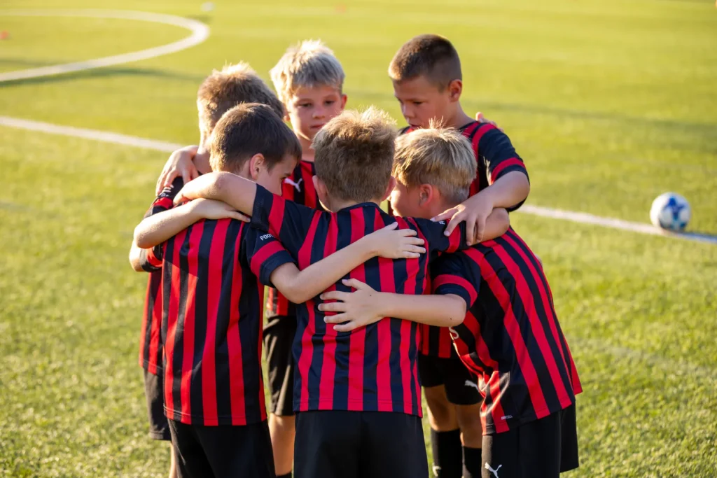 Group of young players in red and black kits hugging in a huddle on the pitch