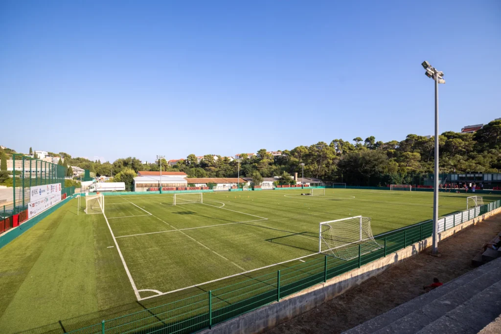 View of the camp football pitch with floodlights and green hillside under a clear blue sky