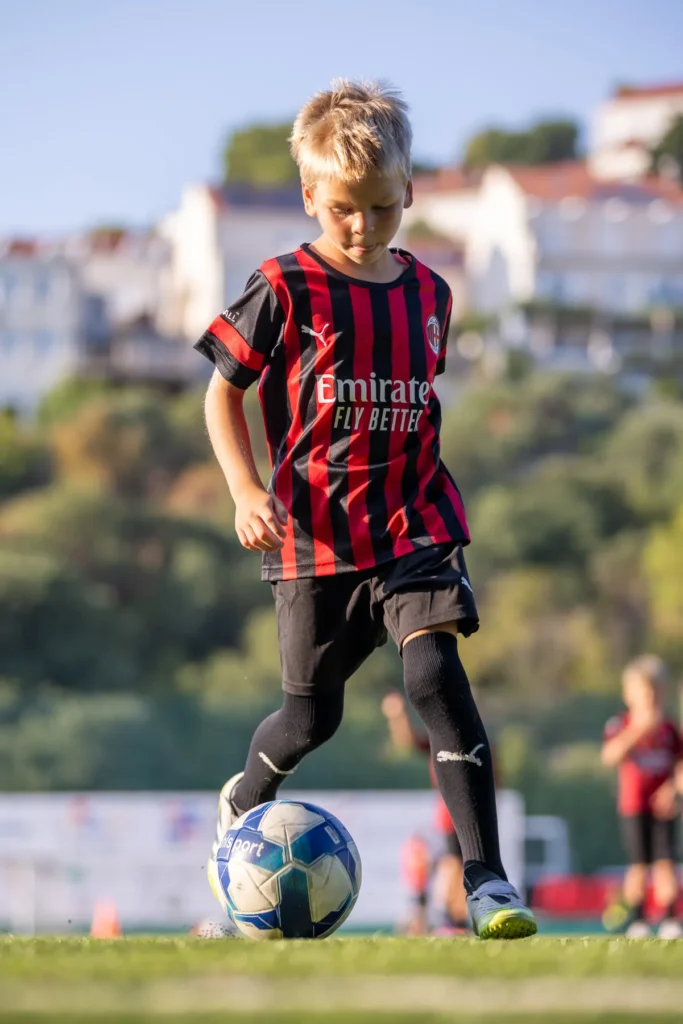 Boy in an AC Milan kit dribbling the ball with blurred houses of Dubrovnik behind him