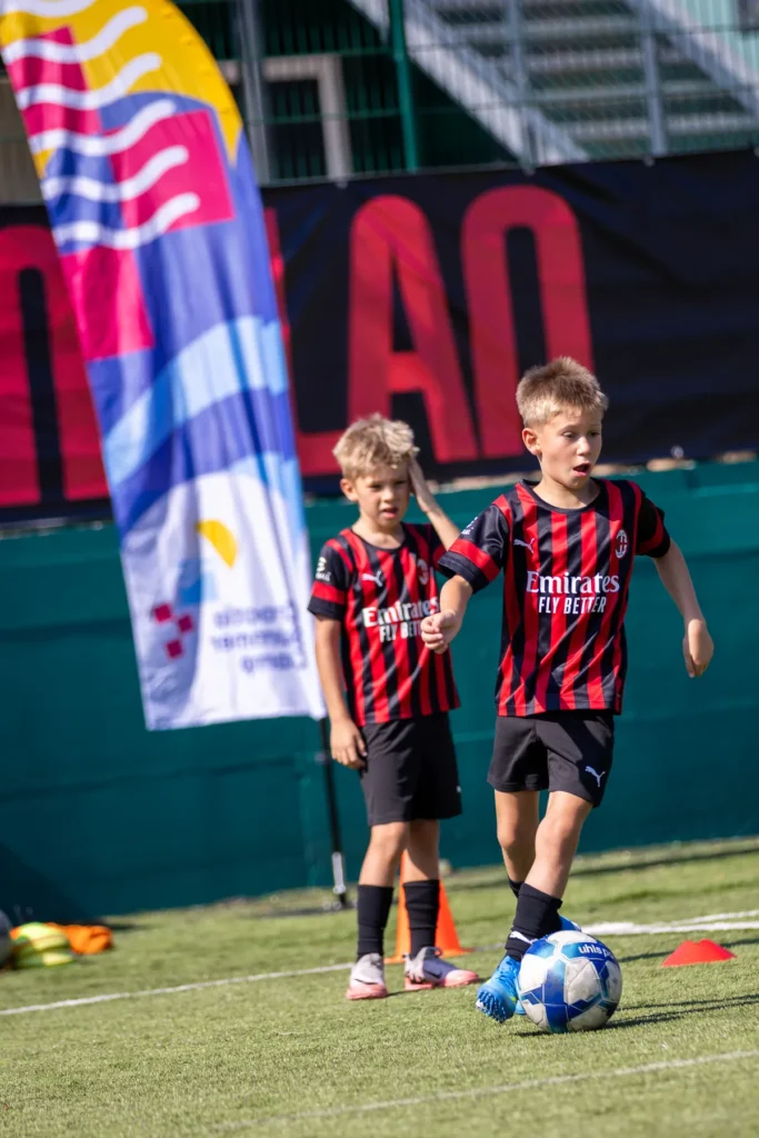 Two young players with a ball next to a colourful camp banner