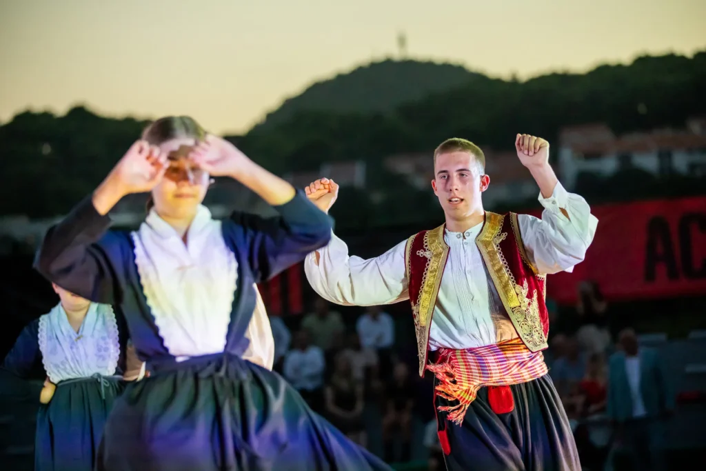 Two folklore dancers in traditional costume performing at dusk during the camp ceremony