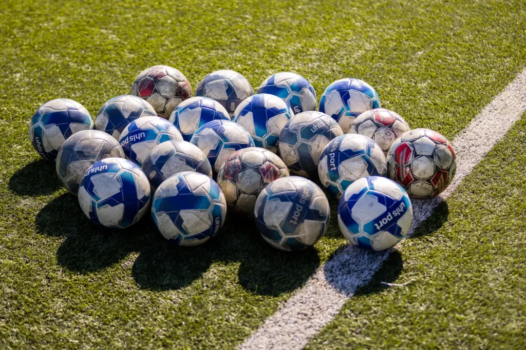 Pile of training footballs on the grass beside a white pitch line