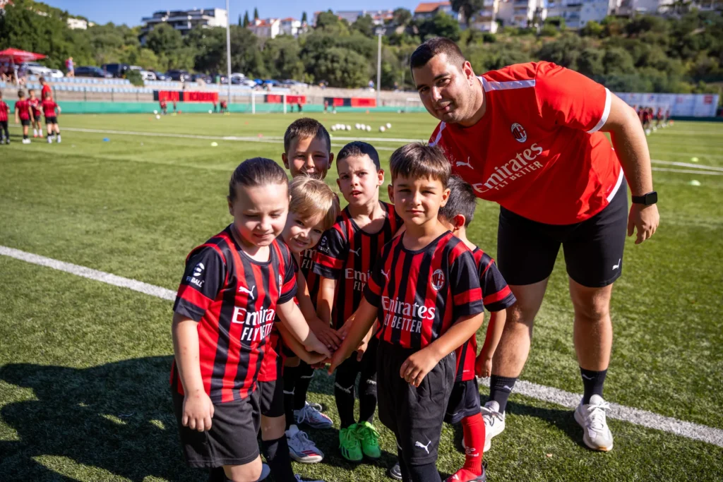 Coach in a red training shirt posing with a group of small children in AC Milan kits