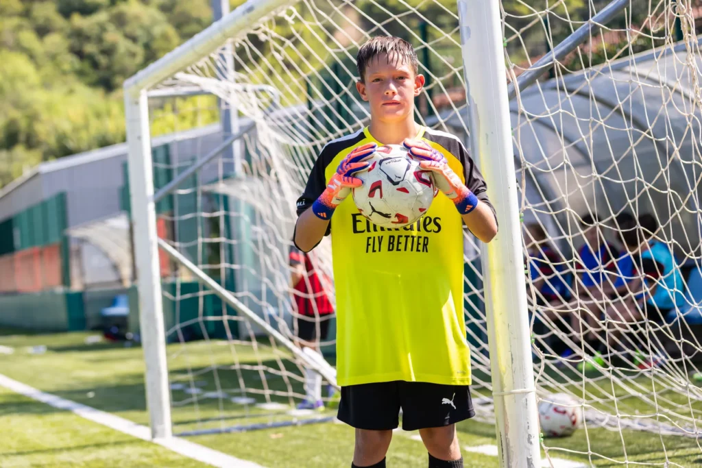 Young goalkeeper in a yellow top holding a football in front of the goal